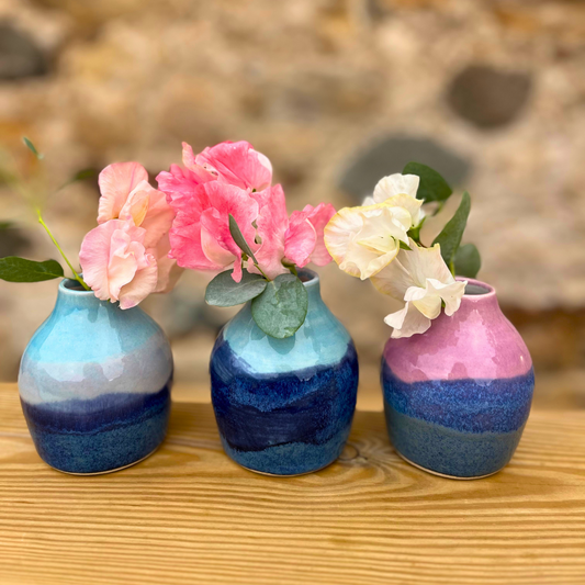 Three small ceramic vases with floral arrangements on a wooden surface.