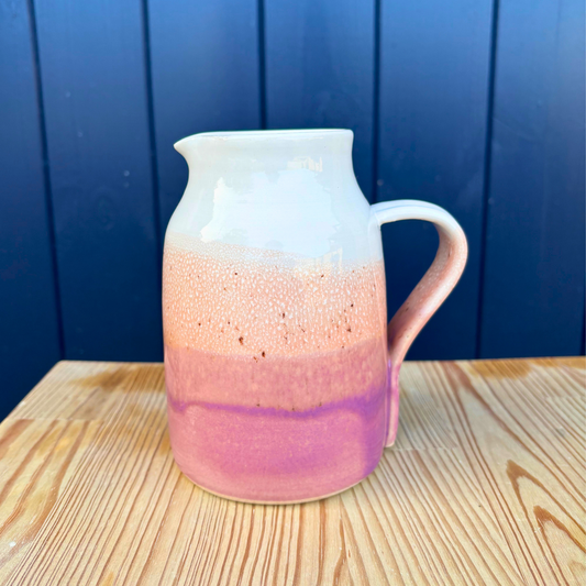 Ceramic pitcher with gradient design on a wooden surface against a blue wall