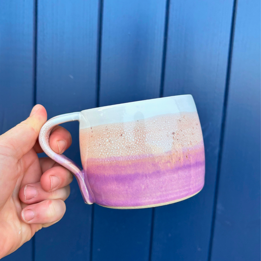 Hand holding a ceramic mug with a gradient design against a blue background