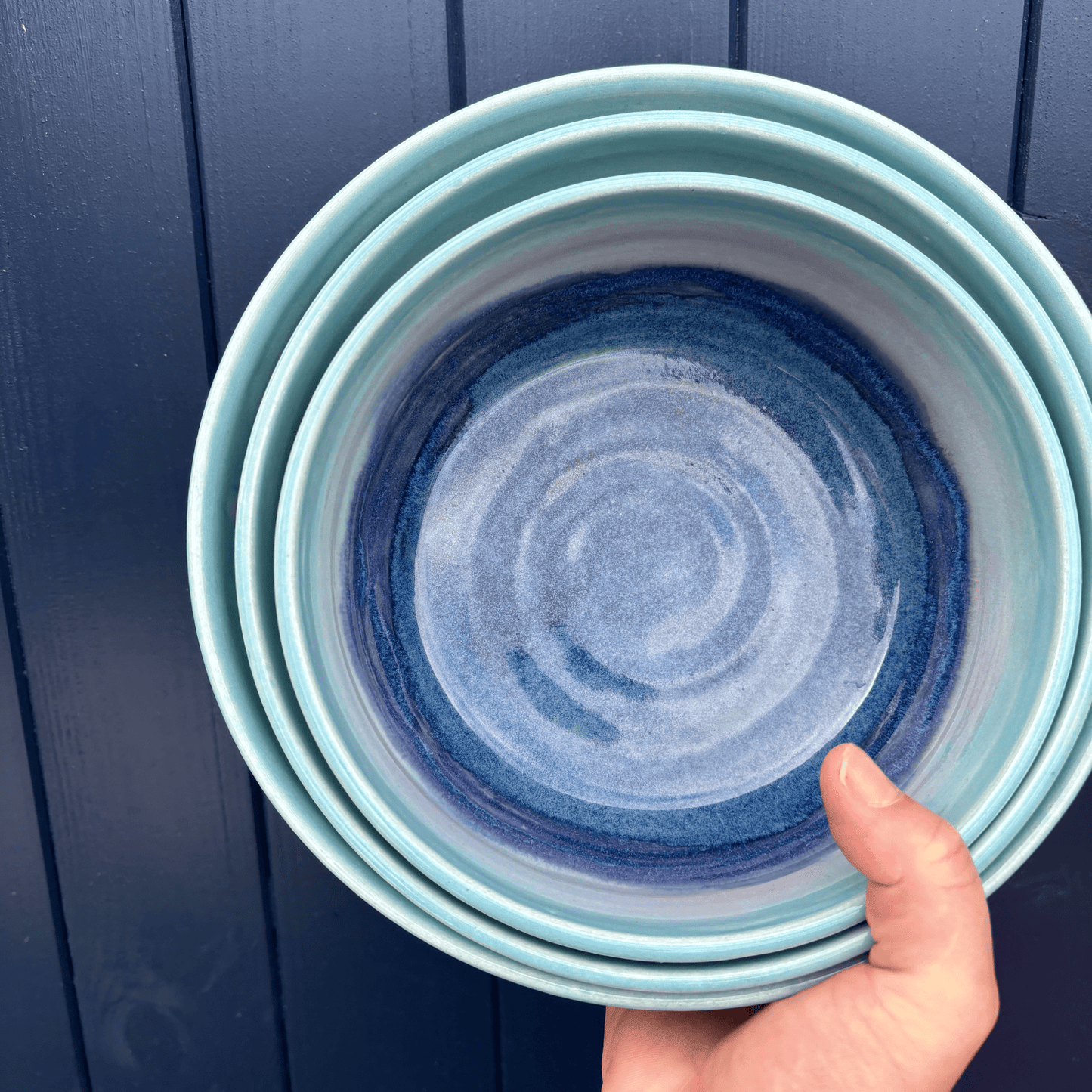 Stack of blue ceramic bowls held against a dark blue wooden background