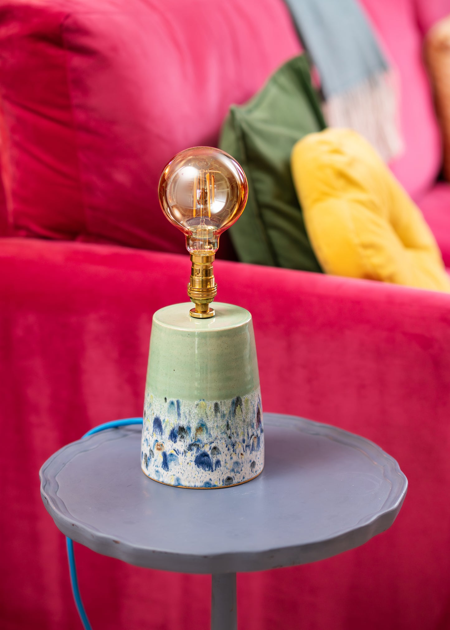 Decorative lamp with a terrazzo base on a small round table against a pink sofa.
