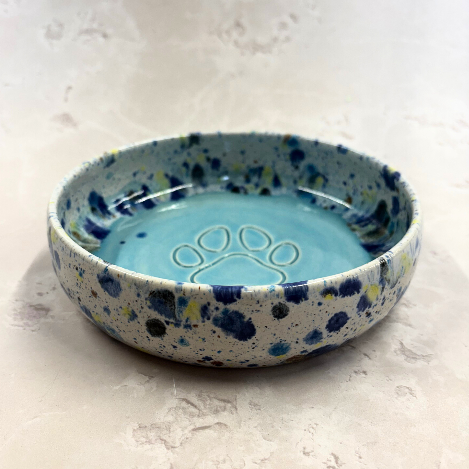 Ella Fletcher Designs handmade  Ceramic bowl with blue speckled exterior and paw print design on a light gray background