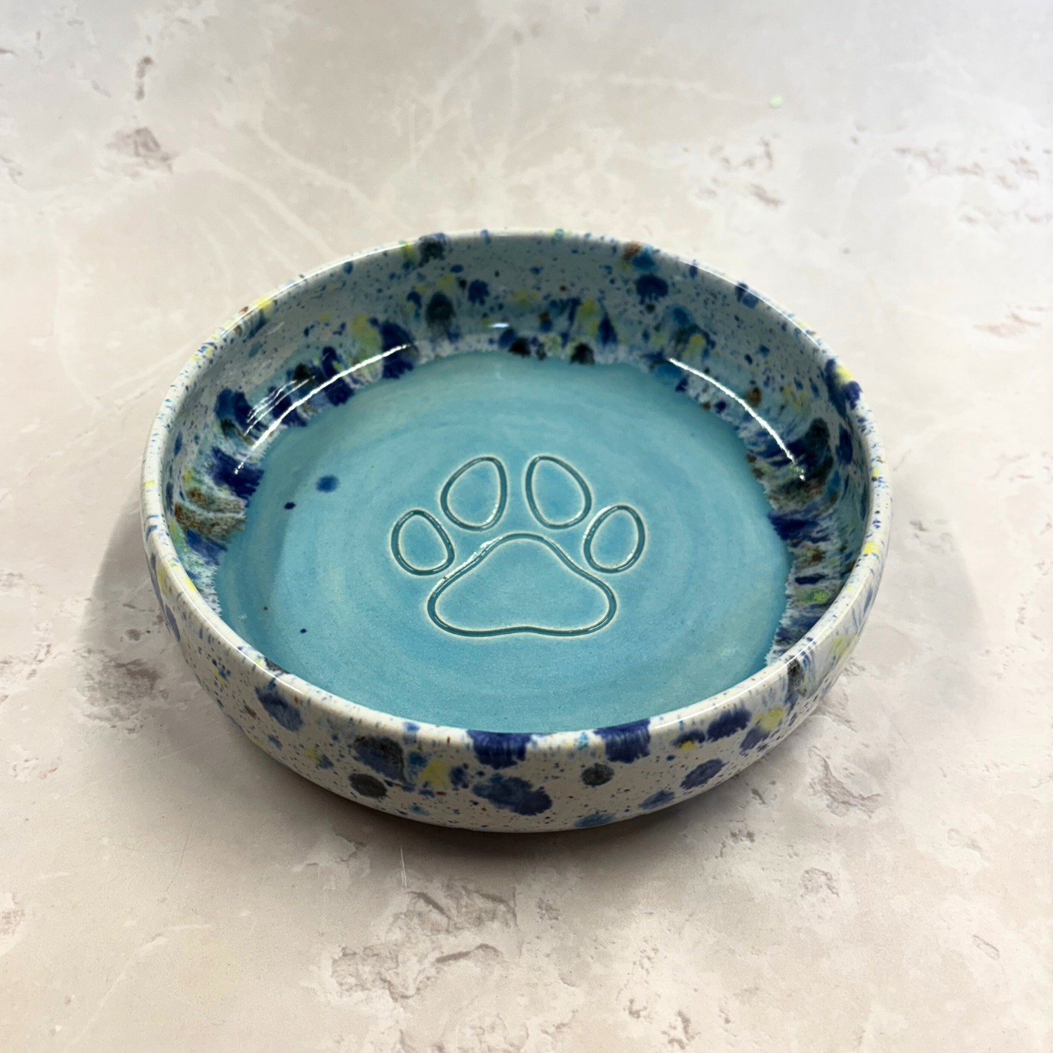 Ella Fletcher Designs handmade  Ceramic bowl with blue speckled exterior and paw print design on a light background
