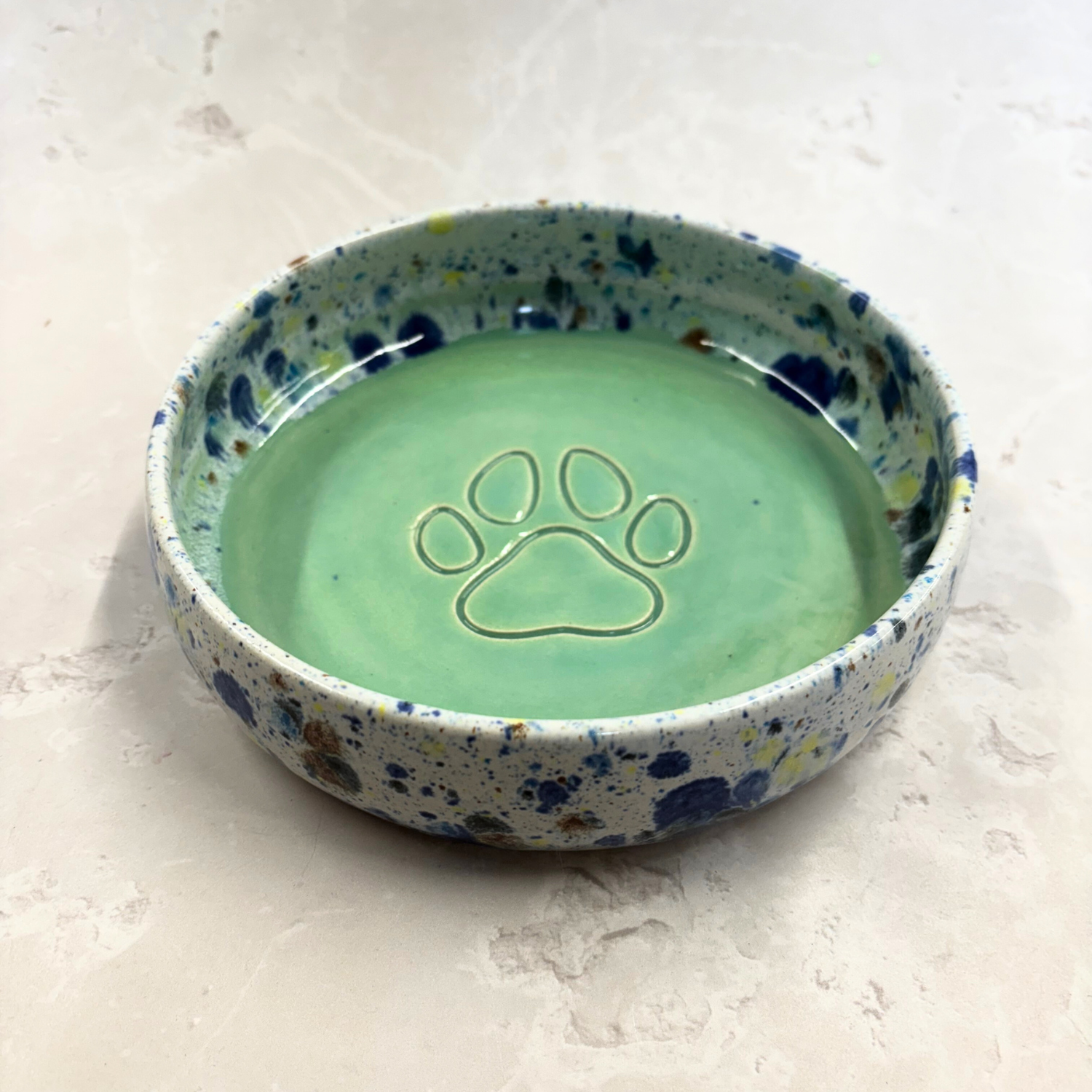 Ella Fletcher Designs handmade  Speckled ceramic bowl with a paw print design on a light background