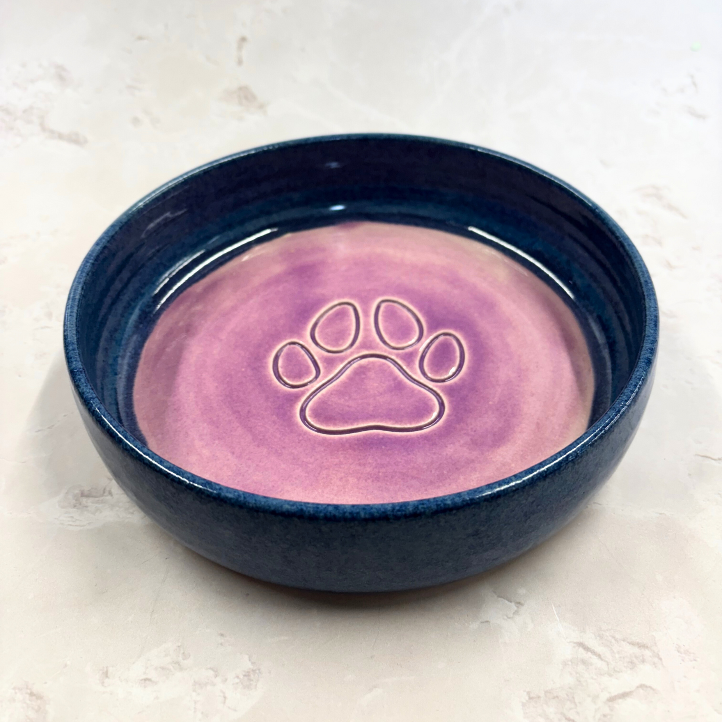 Ella Fletcher Designs handmade  Navy blue ceramic pet bowl with pink interior and paw print design on a light background
