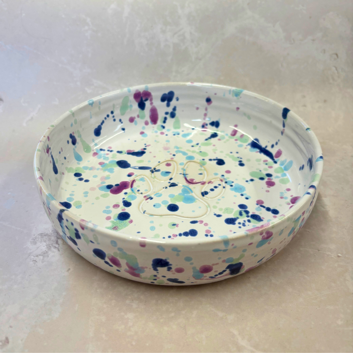 Round ceramic dish with colorful splatter design on a white background