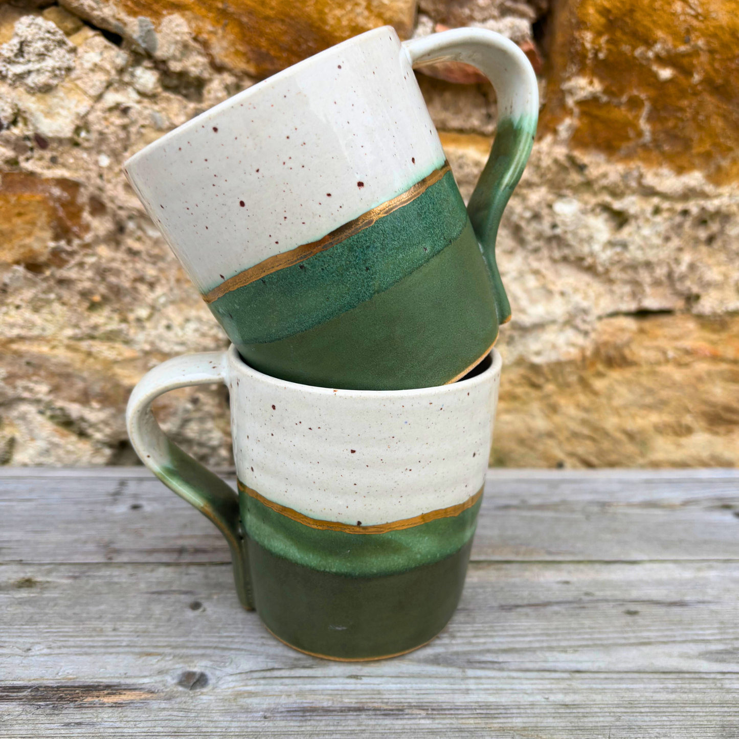 Stack of ceramic mugs with green and white stripes on a wooden surface with stone background