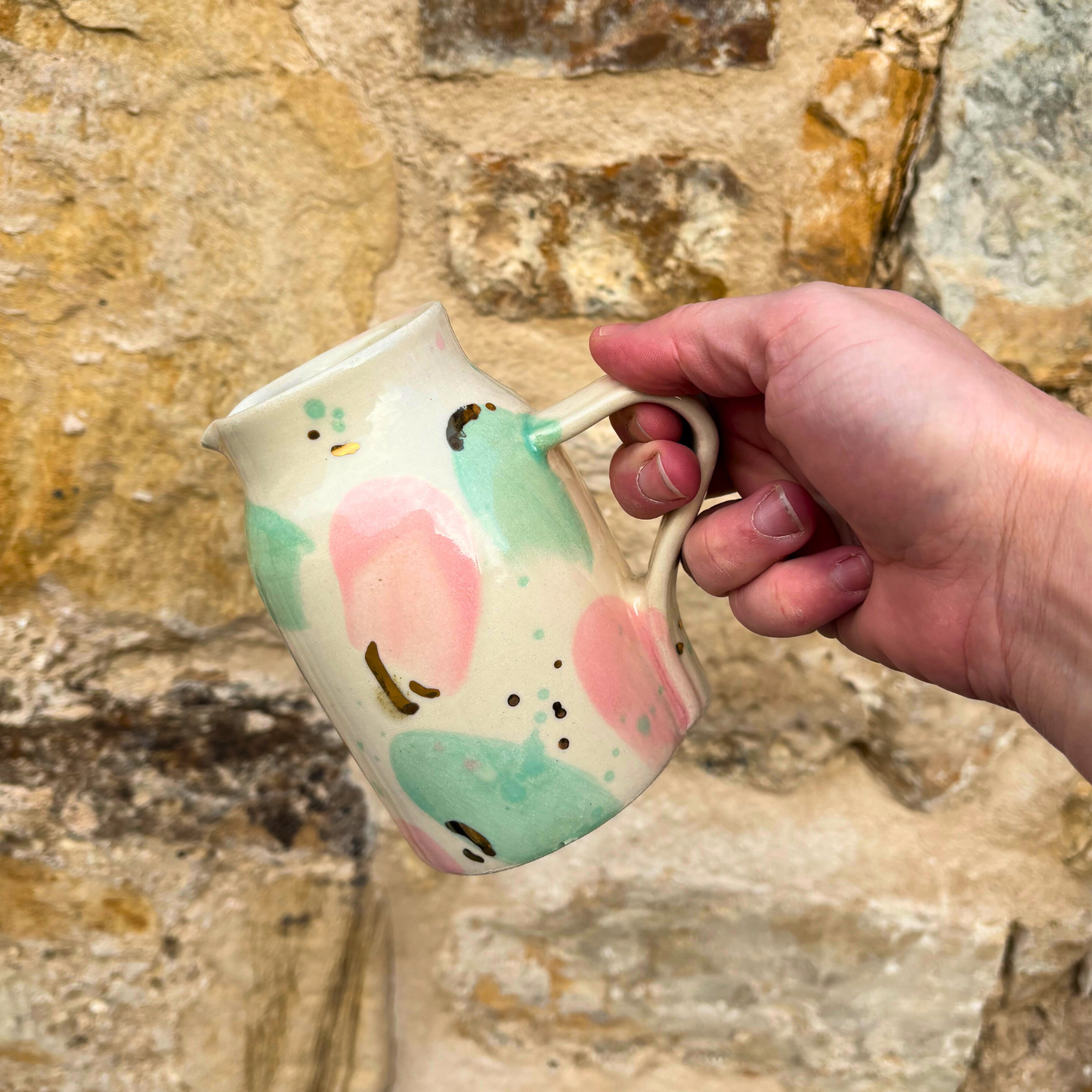 Hand holding a jug with colorful designs against a stone wall background