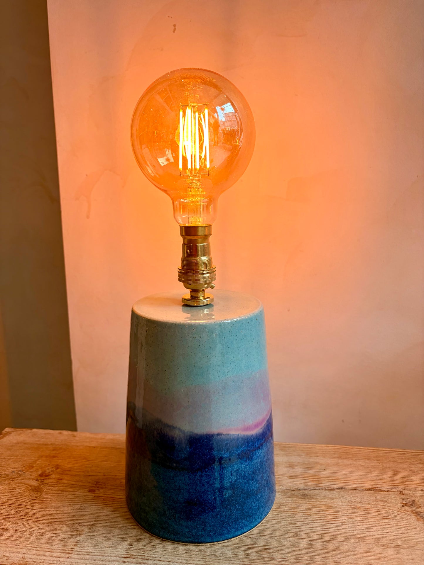 Decorative lamp with a multicolored base and illuminated bulb on a wooden surface.