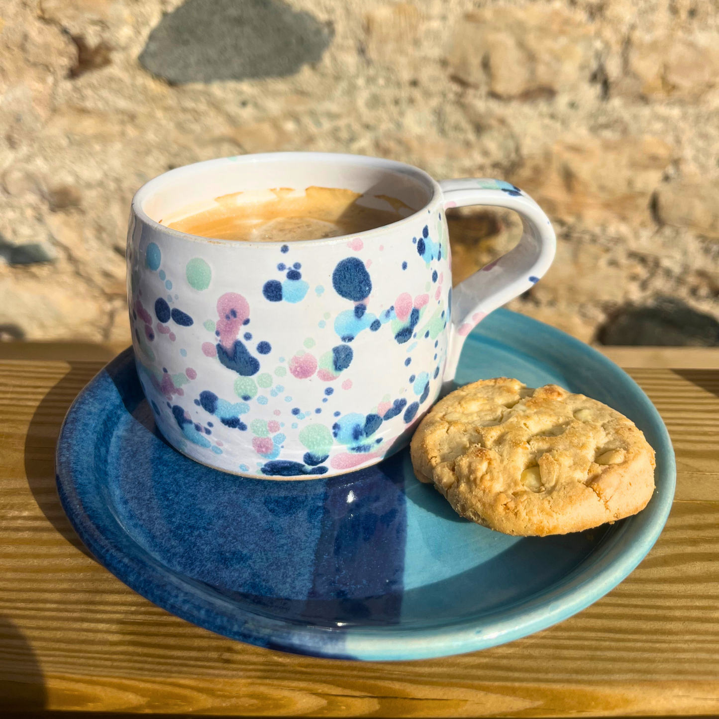 Cup with polka dot design and cookie on a blue saucer against a stone wall background