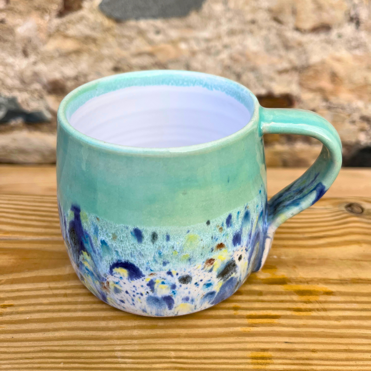 Turquoise ceramic mug with speckled design on a wooden surface