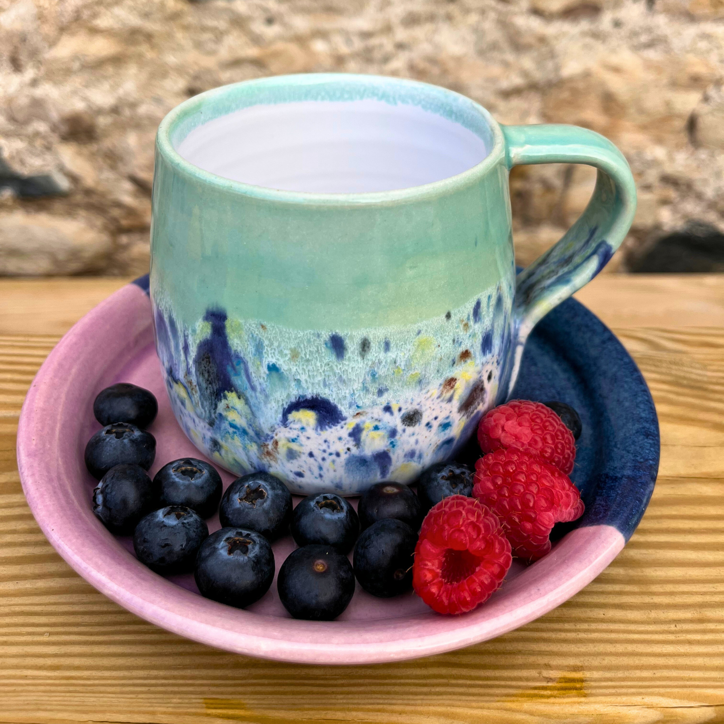 Colorful mug with blueberries and raspberries on a pink plate against a natural stone background