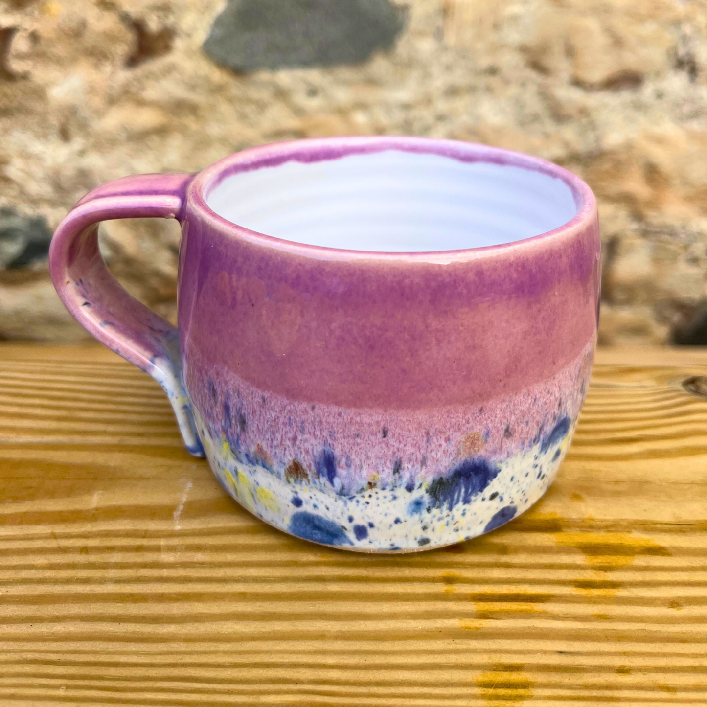 Multicolored ceramic mug on a wooden surface with a natural stone background