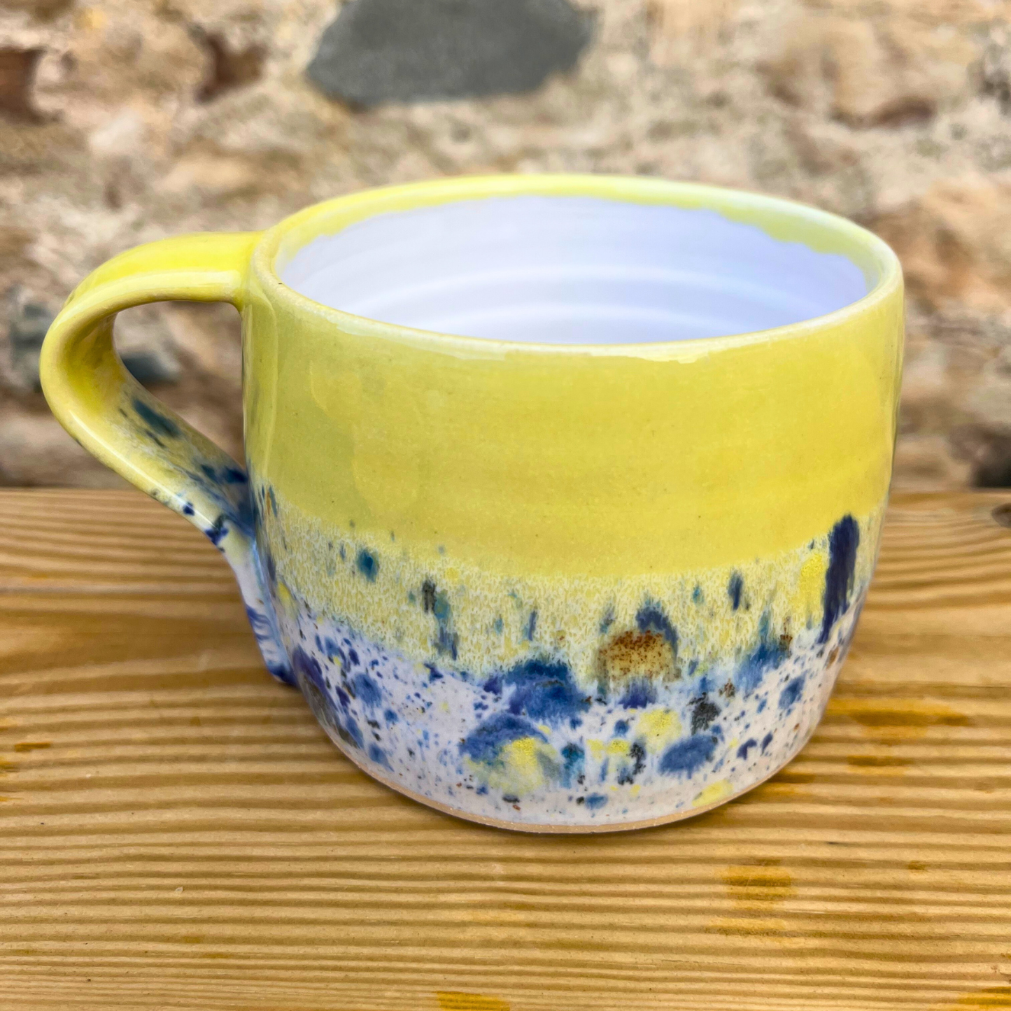 Yellow mug with blue and white speckled design on a wooden surface