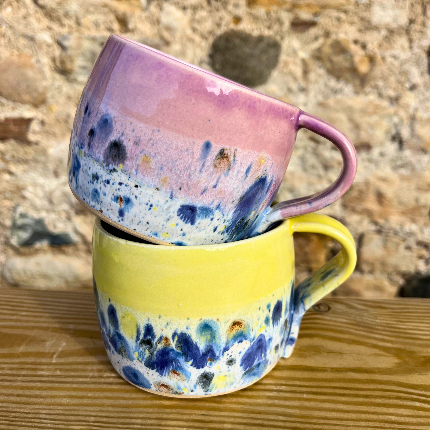 Two ceramic mugs with abstract patterns stacked on a wooden surface.