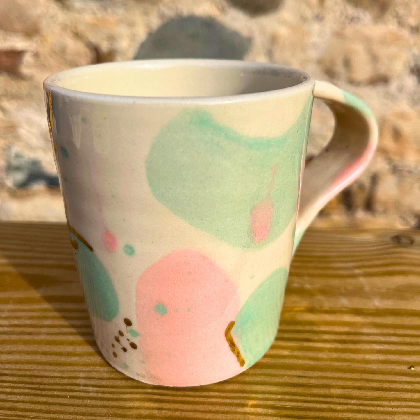 Ceramic mug with abstract green and pink design on a wooden surface