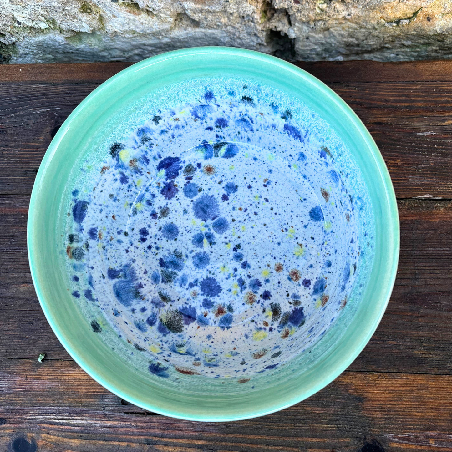 Green ceramic bowl with blue speckled interior on a wooden surface