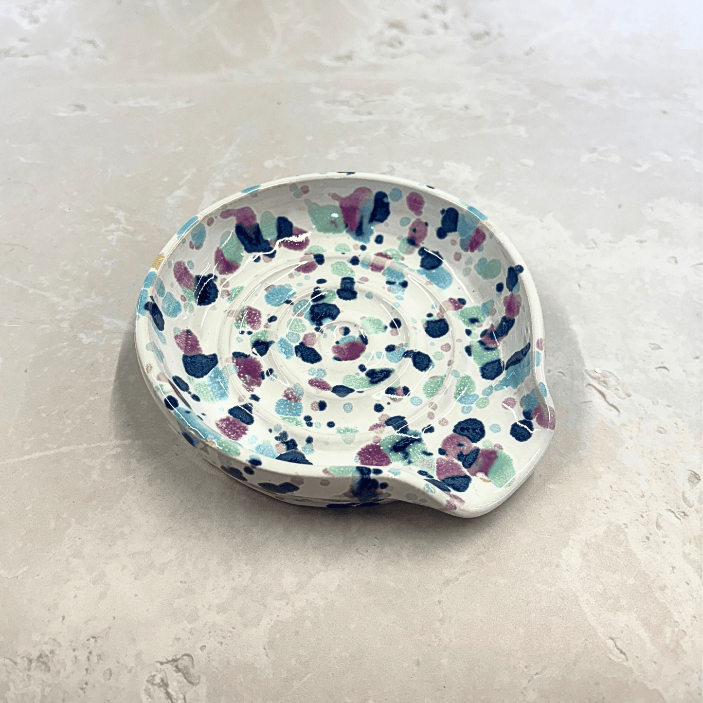Ella Fletcher Designs Handmade UK Ceramic Spoon Rest in Sweetpea design, circular spoon rest with ridges, white background with splattered pinks and blues