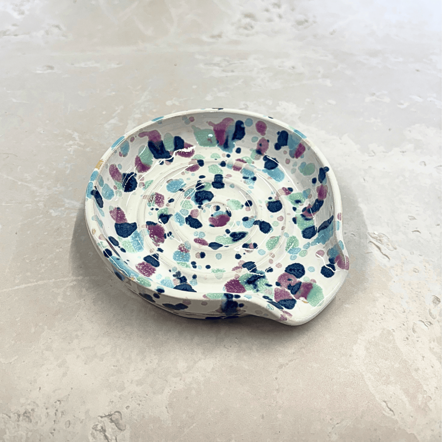 Ella Fletcher Designs Handmade UK Ceramic Spoon Rest in Sweetpea design, circular spoon rest with ridges, white background with splattered pinks and blues