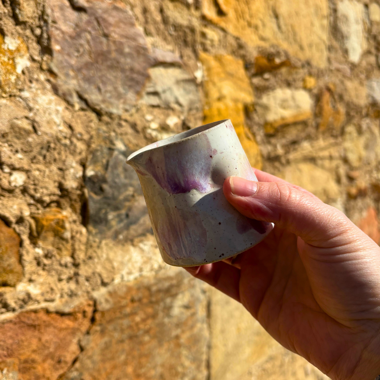 Hand holding a small ceramic cup against a stone wall background