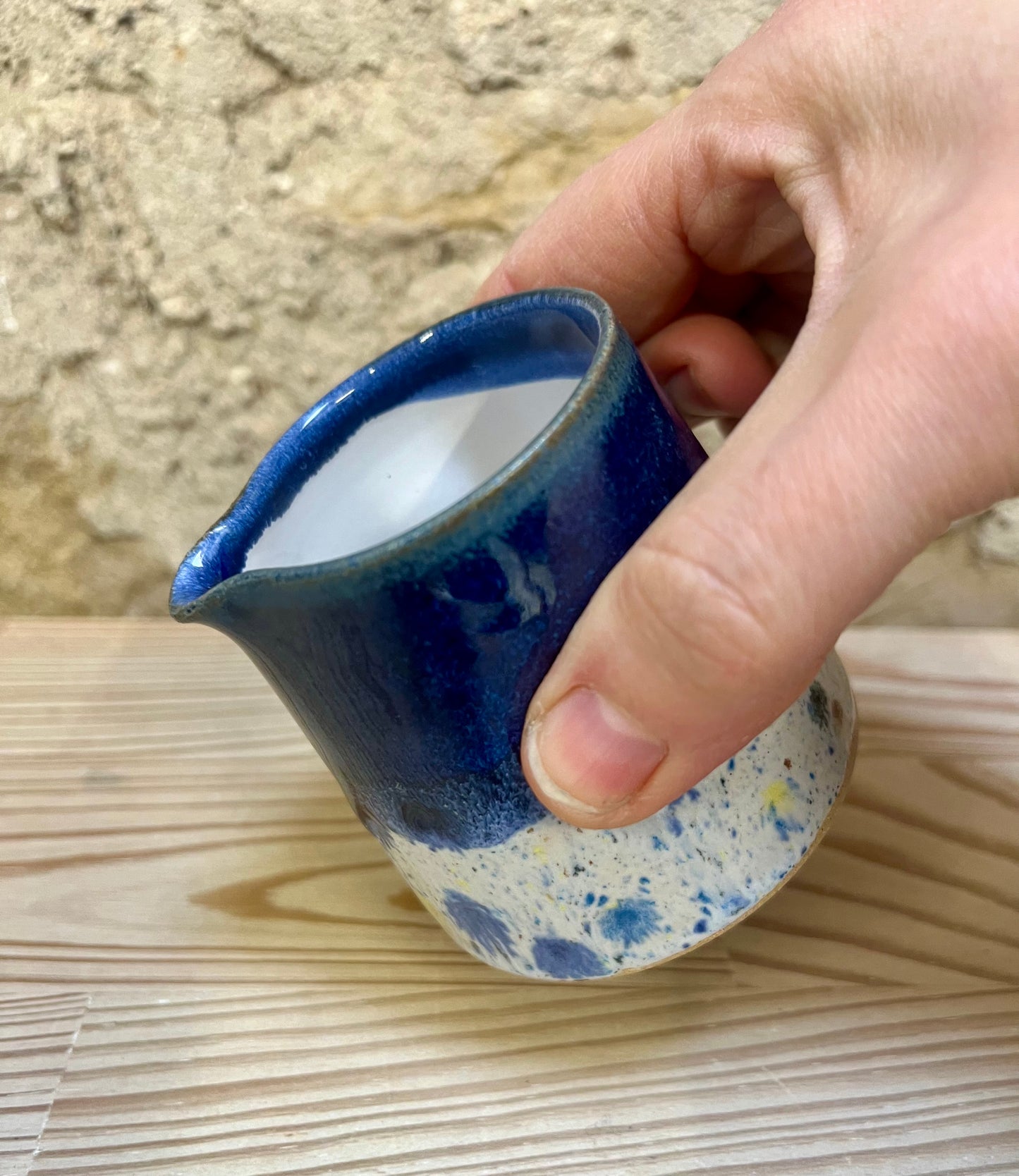 Hand holding a small blue ceramic jug with speckled base on a wooden surface.