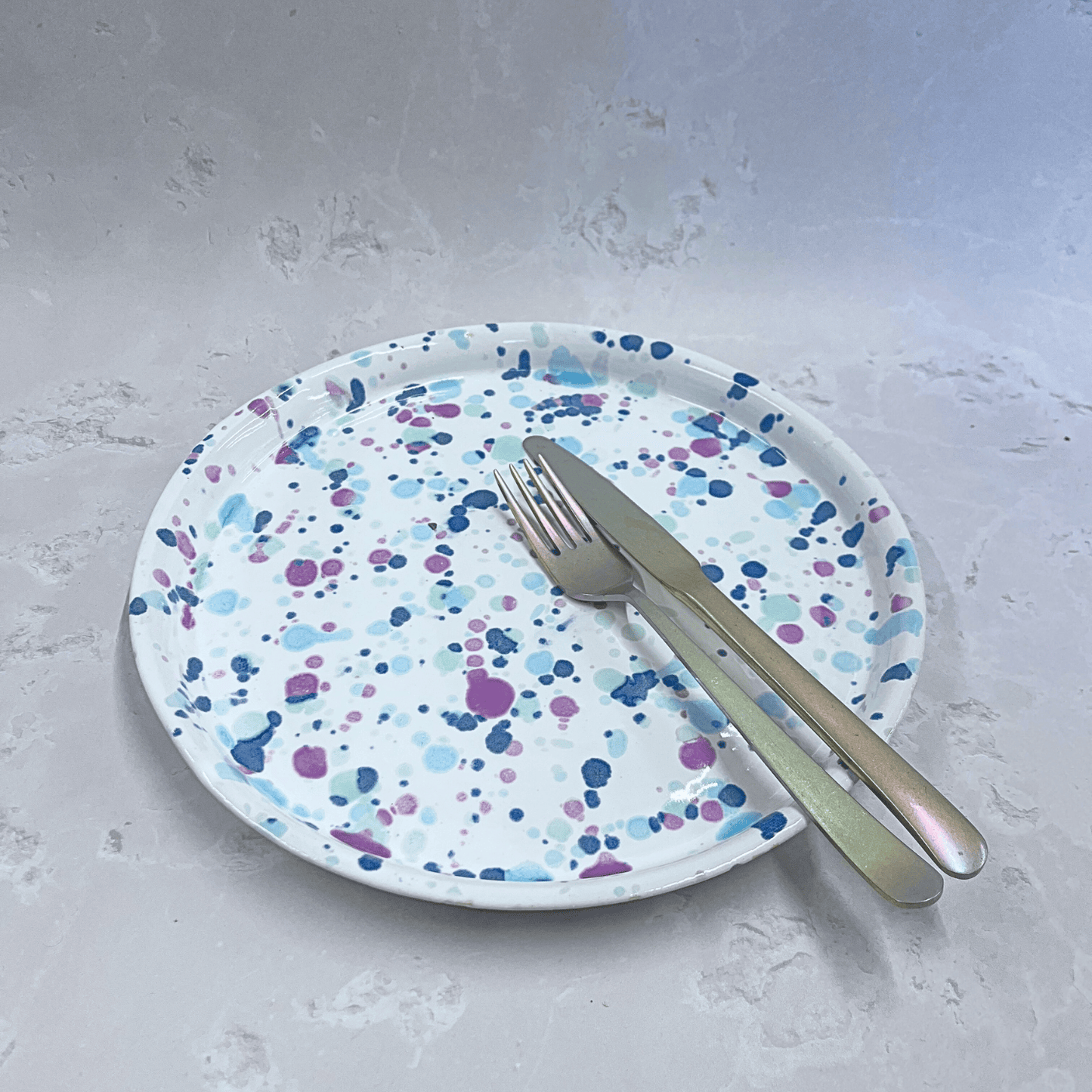 Ella Fletcher Designs Handmade Ceramic Pottery Dinner Plate in Sweetpea design, circular plate with white background speckled with pinks and blues to resemble a sweet pea flower featuring a fork and knife for scale