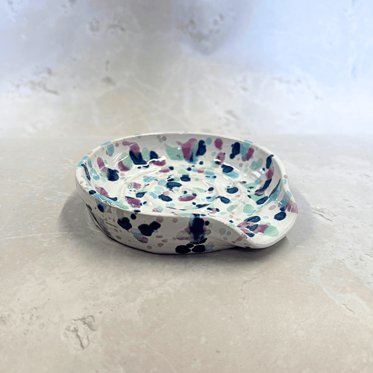 Ella Fletcher Designs Handmade Ceramics Spoon Rest in Sweetpea design, circular spoon rest with ridges, white background with splattered pinks and blues