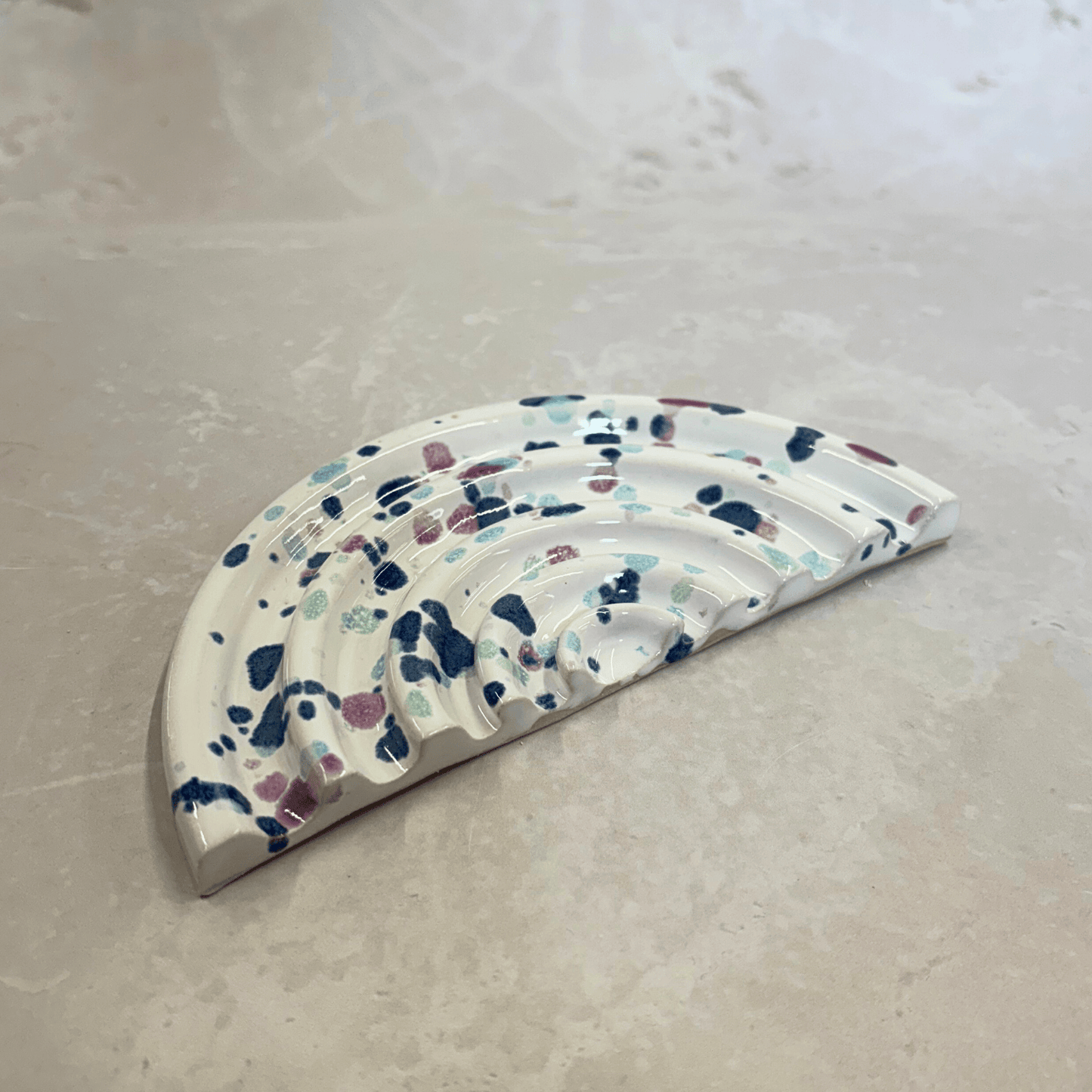 Ella Fletcher Designs UK Handmade Ceramics Soap Dish in Sweetpea, semi-circle dish with ridges, white background with splatters of blues and pinks