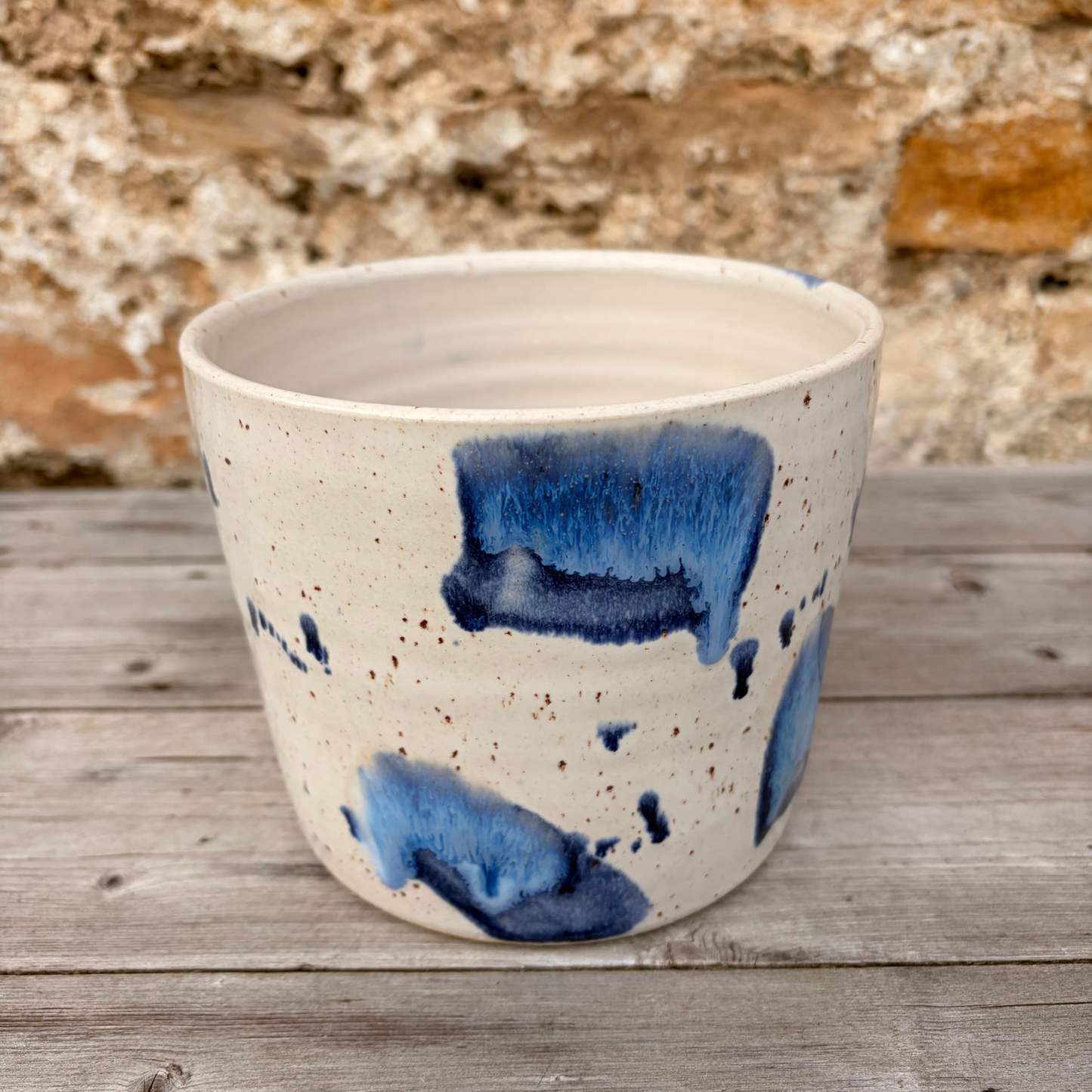 Ceramic pot with blue abstract design on a wooden surface with stone wall background