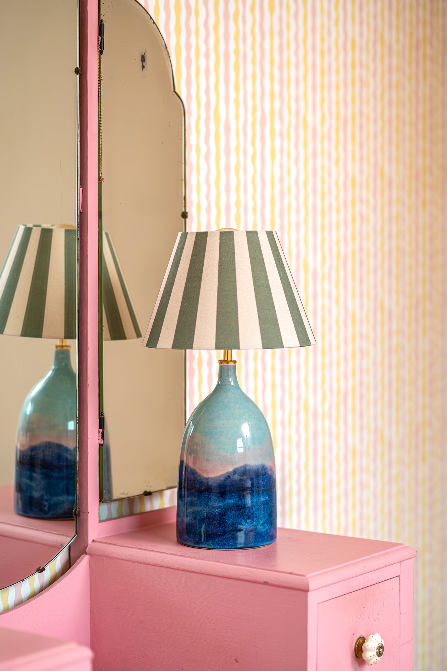 Blue lamp with striped shade on a pink cabinet against a striped wall