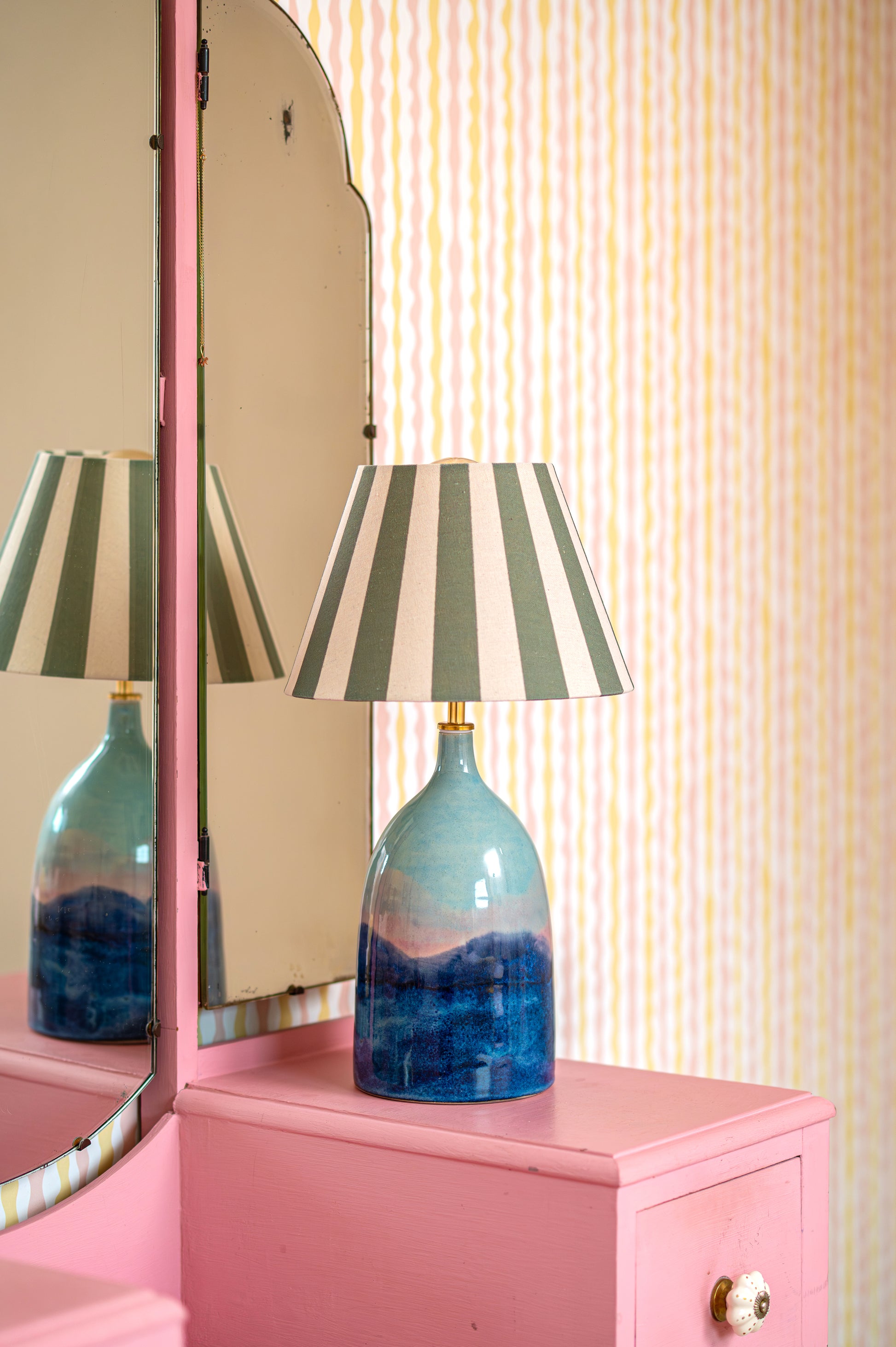 Blue lamp with striped shade on a pink cabinet against a striped wall
