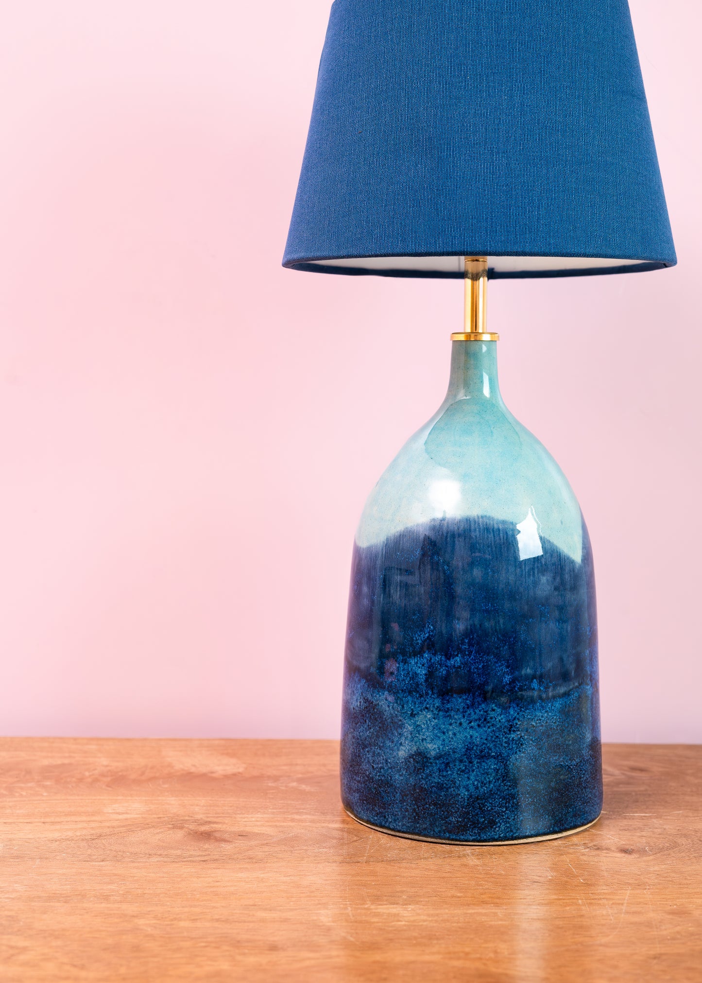 Blue ceramic table lamp with a matching shade on a wooden surface against a pink background