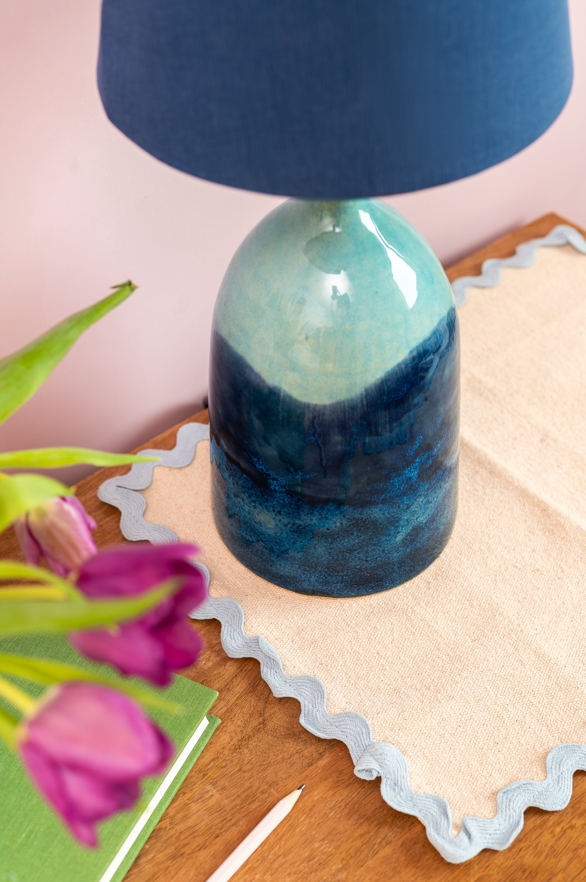 Blue and green ceramic lamp on a wooden surface with pink tulips