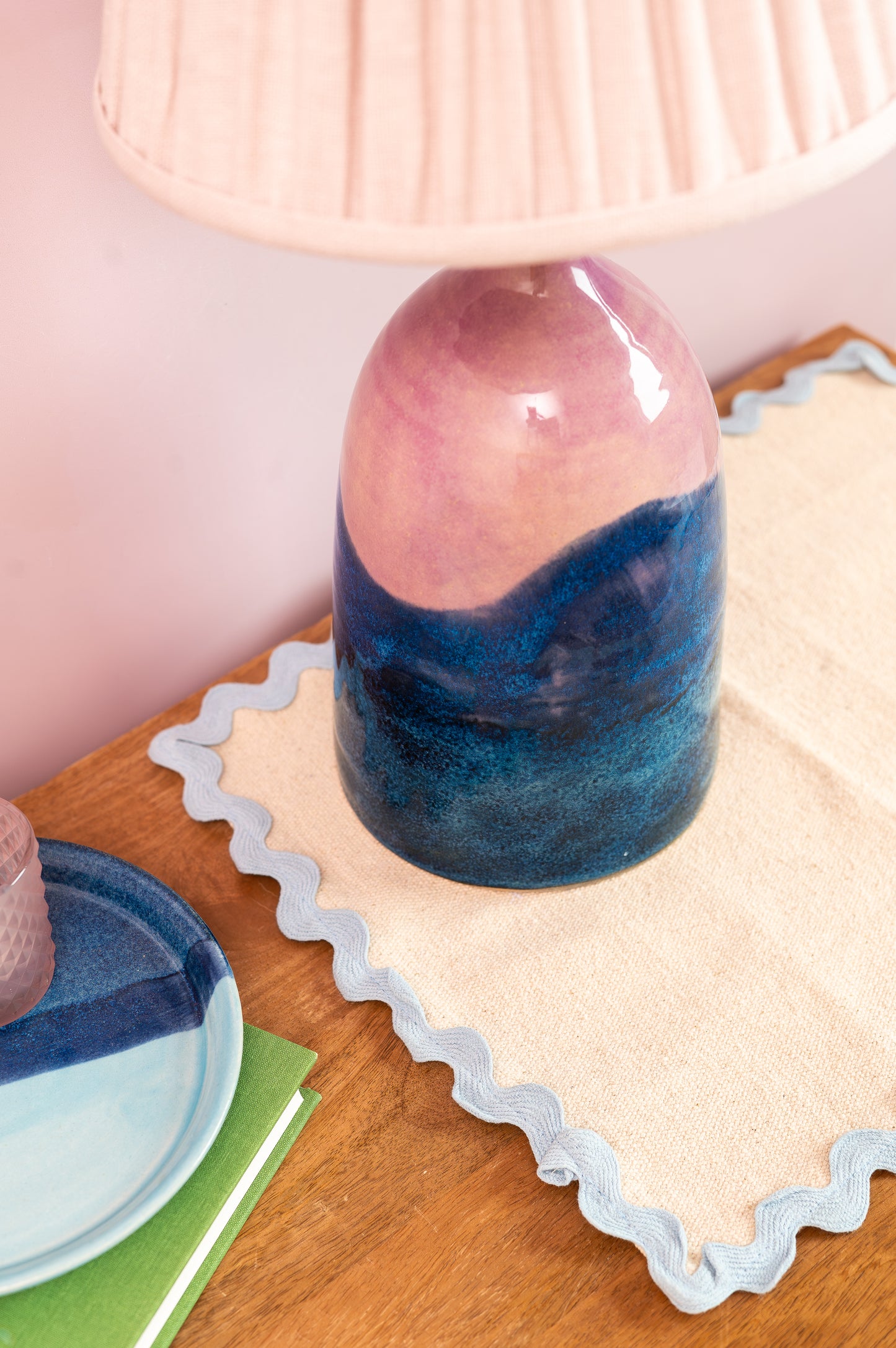 Decorative vase with gradient design on a wooden surface with a lamp in the background