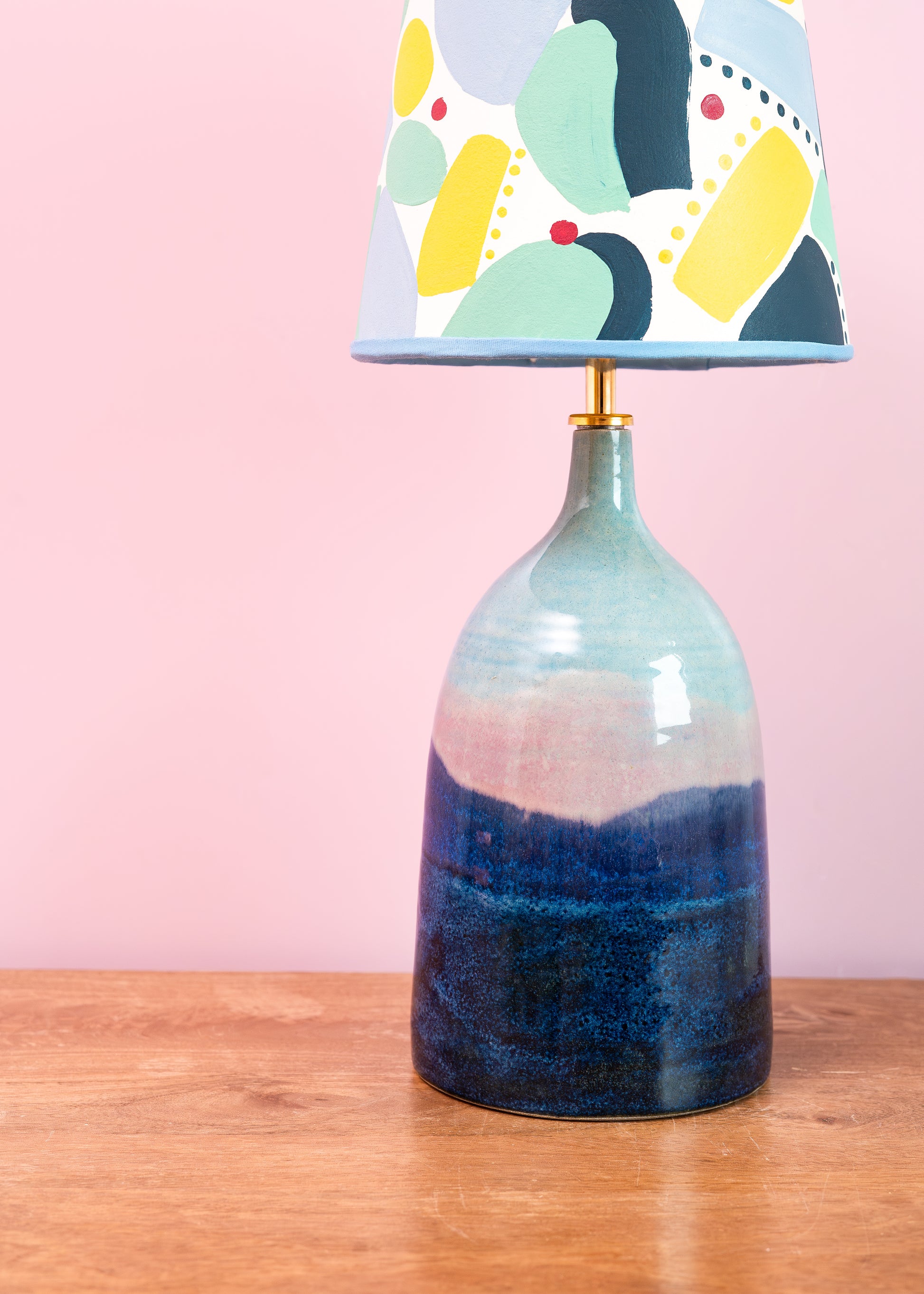 Table lamp with a colorful lampshade on a wooden surface against a pink background