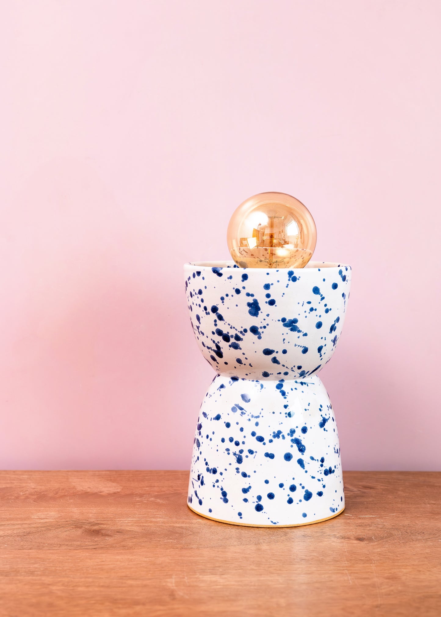 Decorative lamp with blue speckled base and gold shade on a wooden surface with pink background