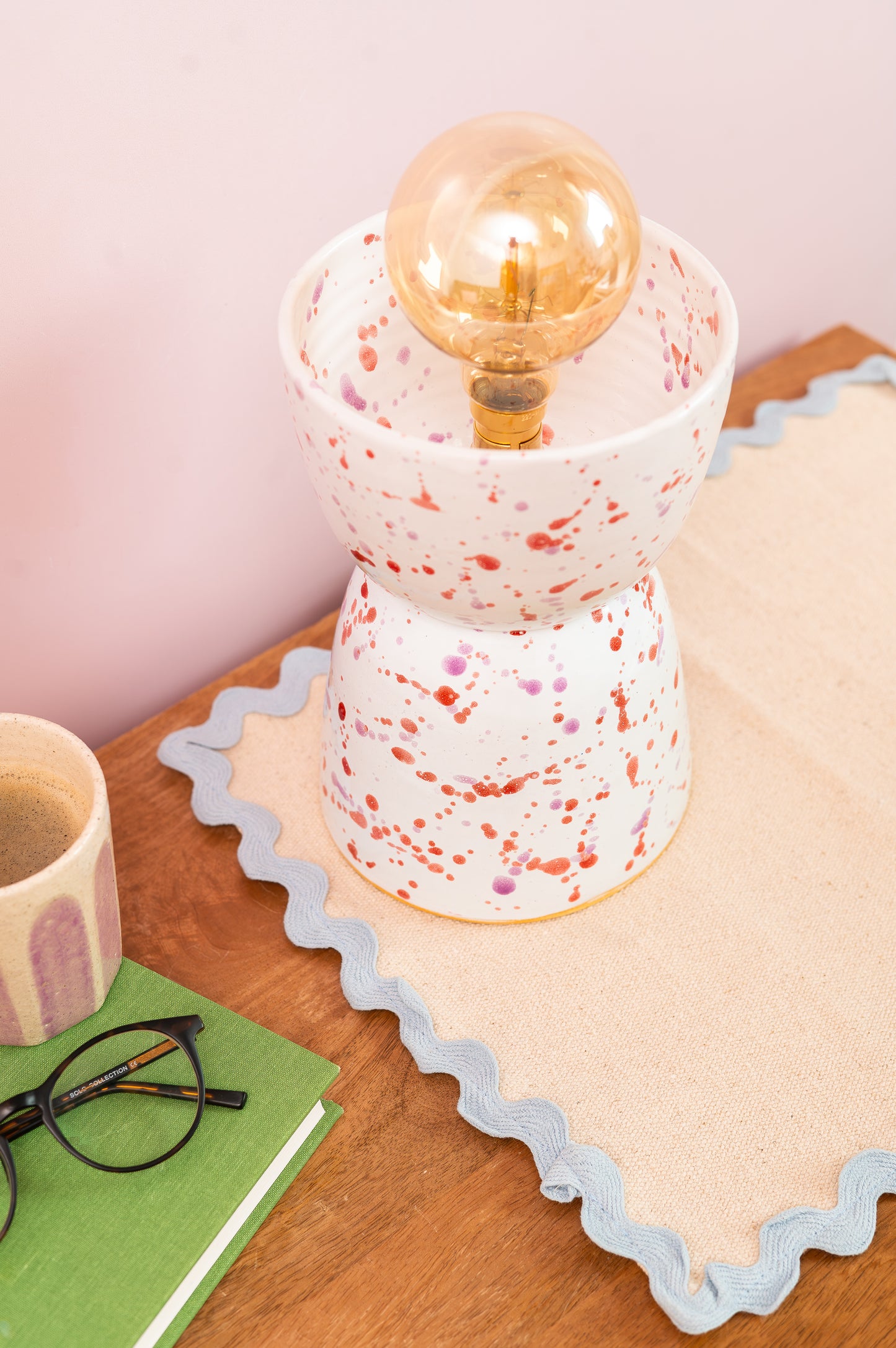 Speckled ceramic lamp with a gold bulb on a wooden surface with a pink background