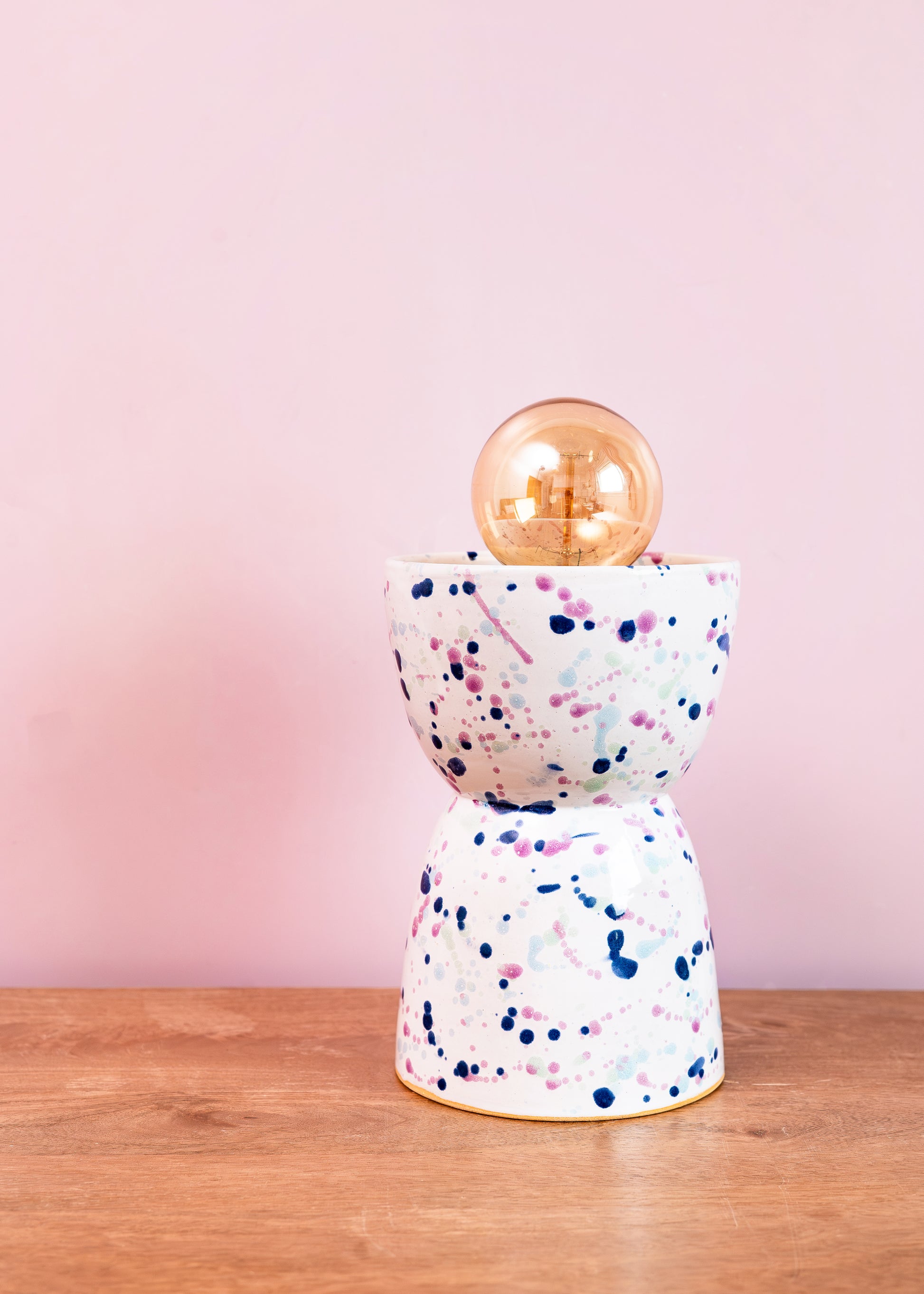 Decorative lamp with terrazzo design and gold bulb on a wooden surface with pink background
