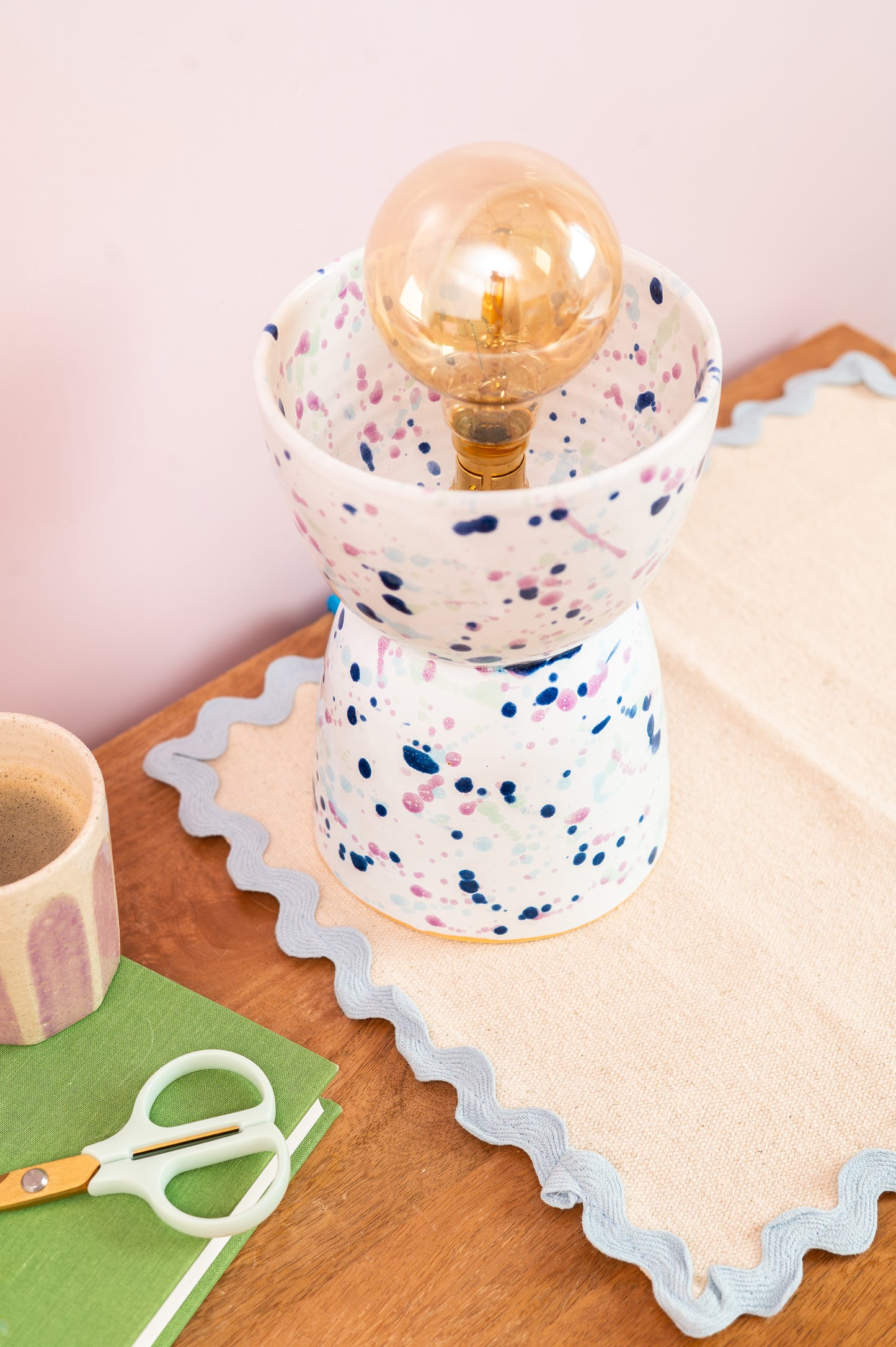 Speckled ceramic lamp with a gold bulb on a wooden surface with a pink background
