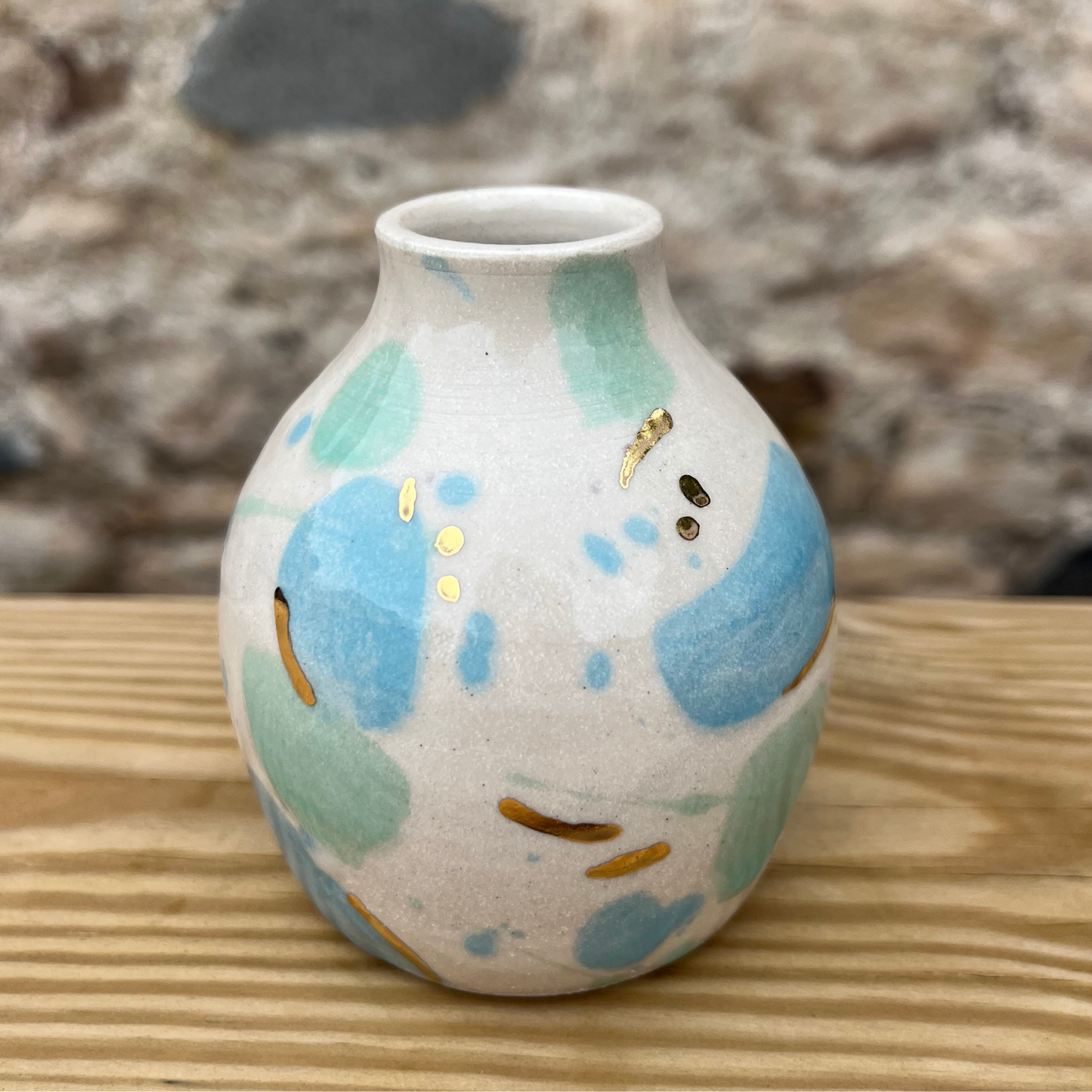 Small ceramic vase with blue and green abstract patterns on a wooden surface