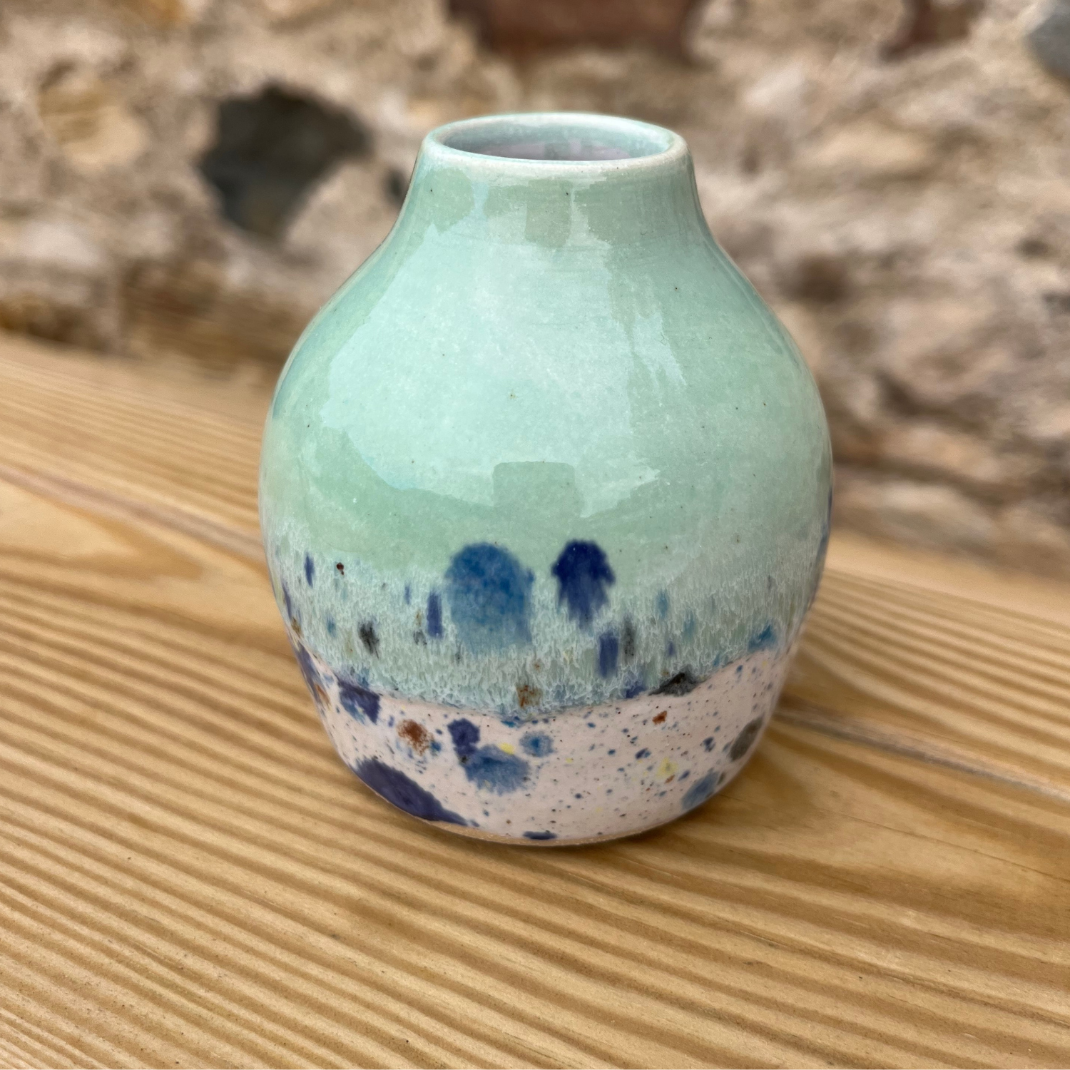Green ceramic vase with speckled design on a wooden surface