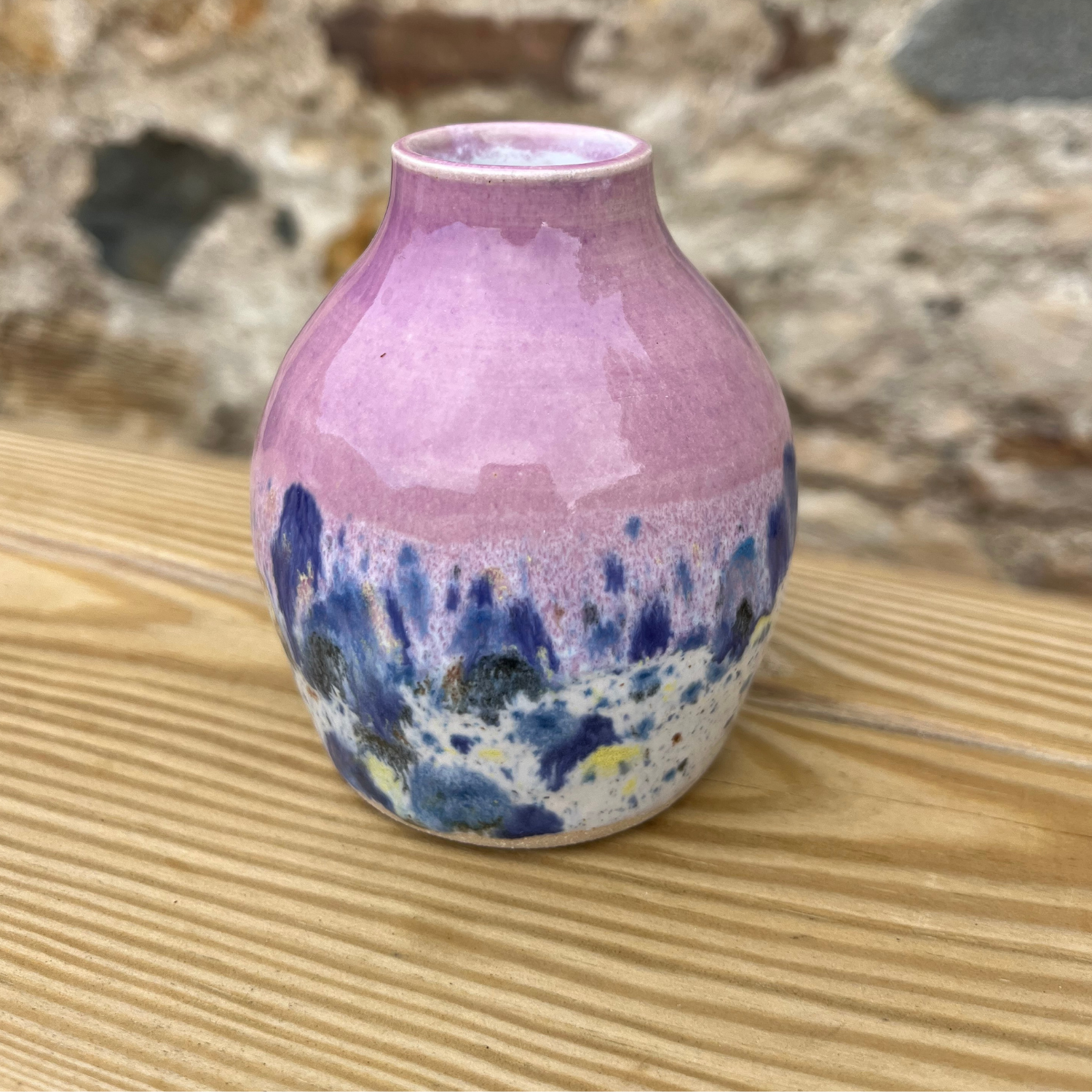 Pink and blue ceramic vase on a wooden surface with a natural background