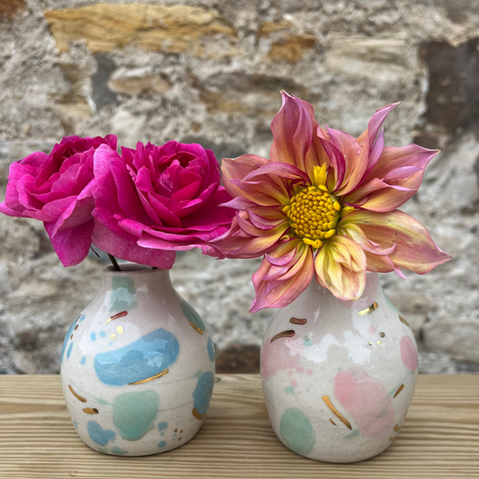 Two small ceramic vases with floral arrangements against a stone wall background