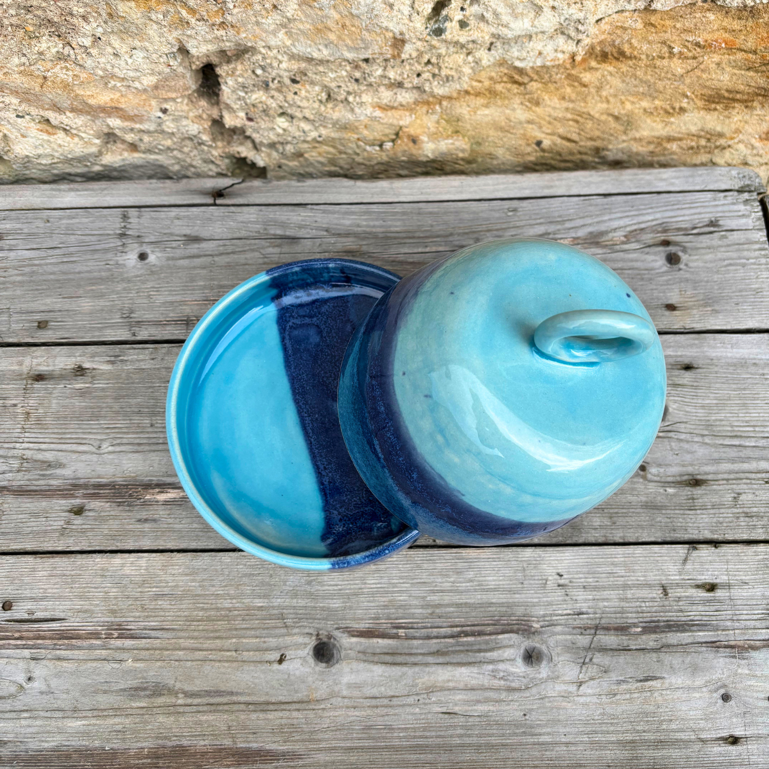 Two blue ceramic containers on a wooden surface with a stone background