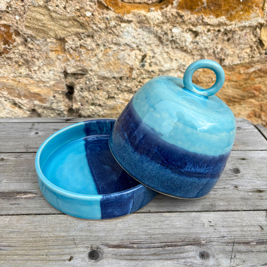 Blue ceramic container with a lid on a wooden surface against a stone wall background