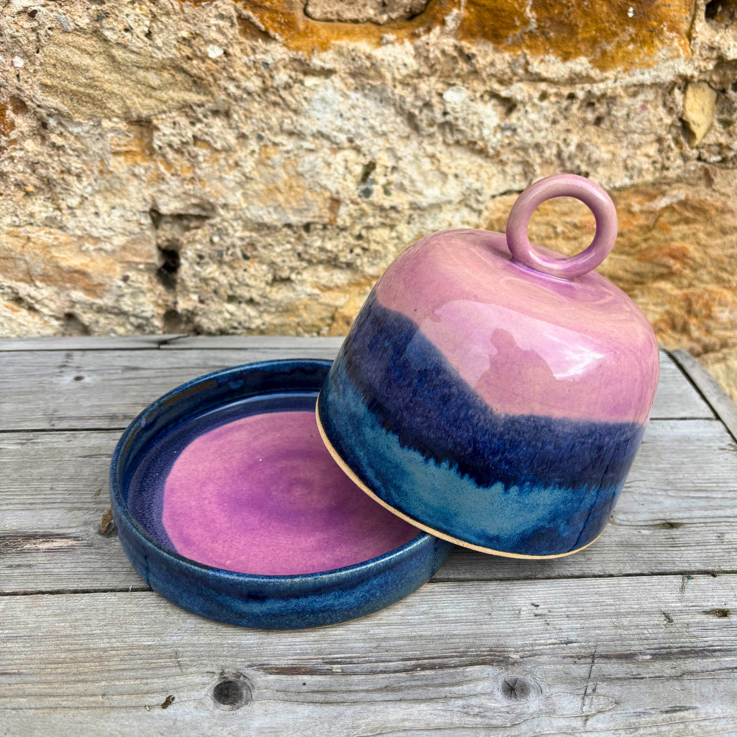Ceramic dish with a lid featuring pink and blue glaze on a wooden surface.