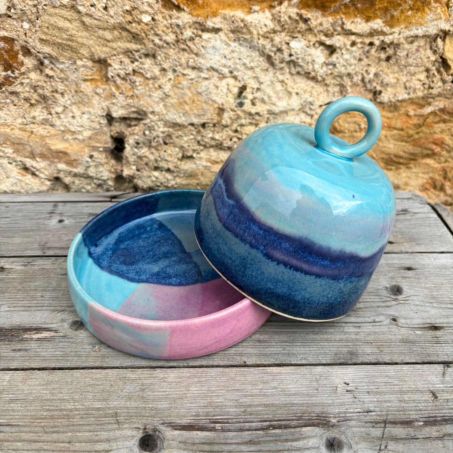 Ceramic jar with a lid featuring blue and pink gradient on a wooden surface.