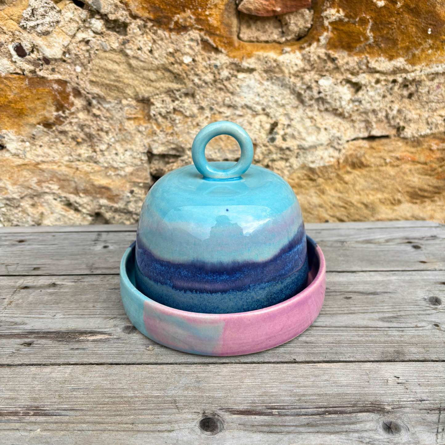 Ceramic butter dish with a lid on a wooden surface against a stone wall background