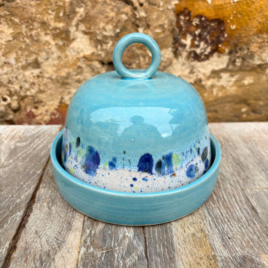 Blue ceramic cheese dome with speckled pattern on a wooden surface