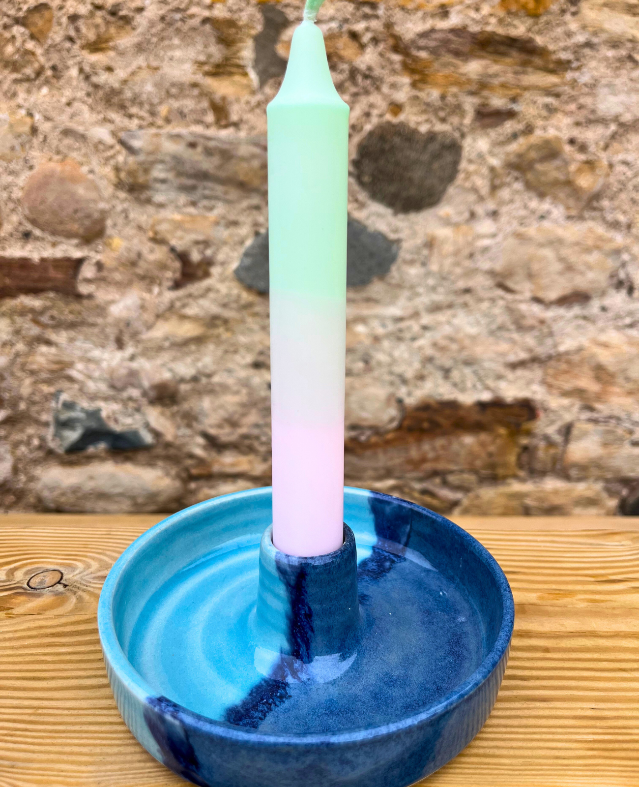Tall green candle in a blue ceramic holder against a stone wall background